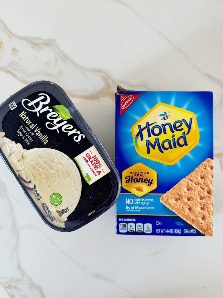 A container of Breyers natural vanilla ice cream is next to a box of Honey Maid graham crackers on a marble countertop.