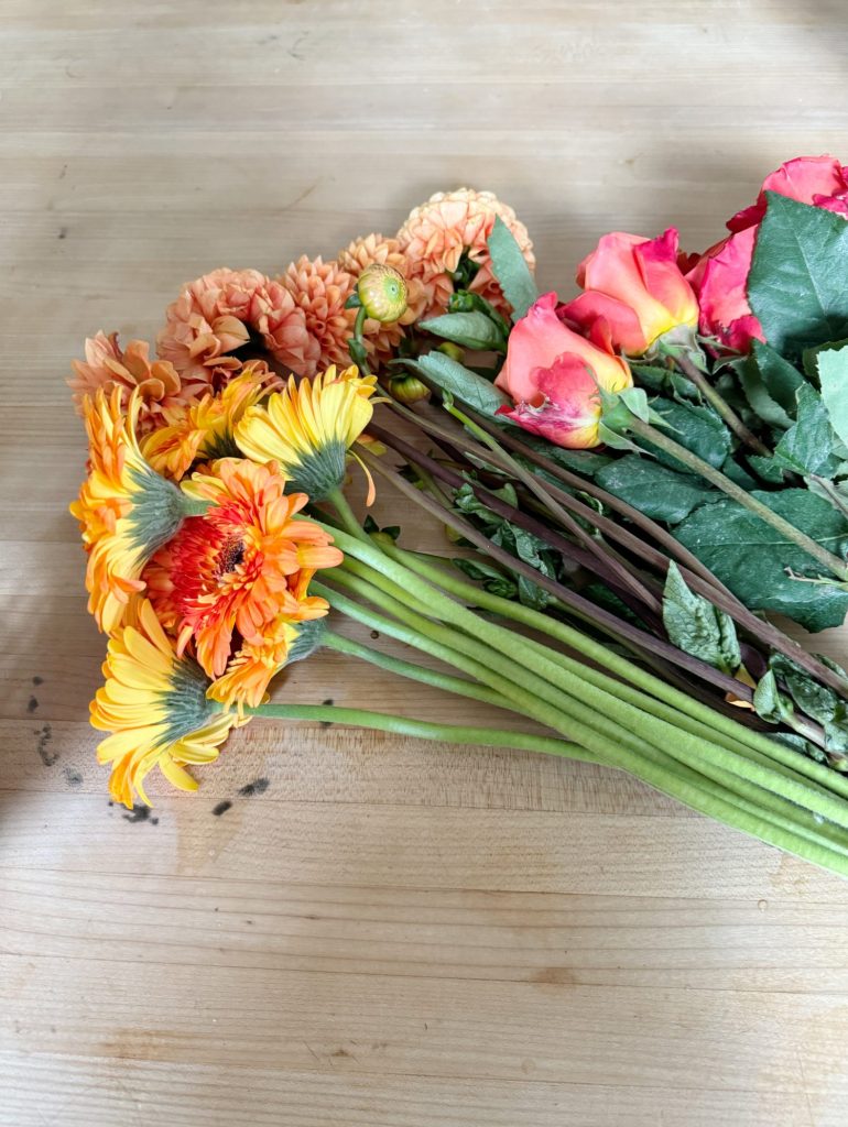 A bouquet of mixed flowers including orange and pink blooms, resting on a wooden surface.