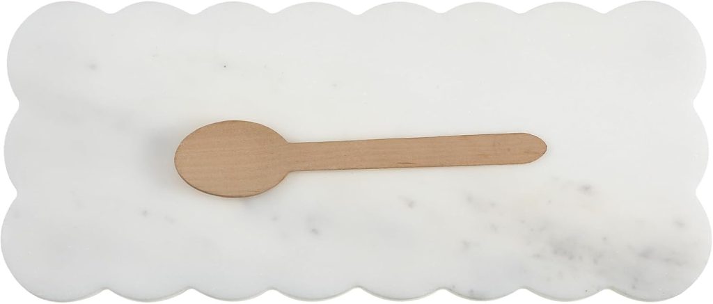 A small wooden spoon rests horizontally on a rectangular white marble slab with scalloped edges, ready to serve delicate apple tartlets.