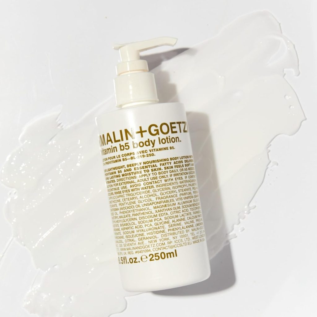 A white pump bottle of Malin + Goetz Vitamin B5 Body Lotion lies on a smear of white lotion, photographed on a white background—an ideal house guest gift for any occasion.