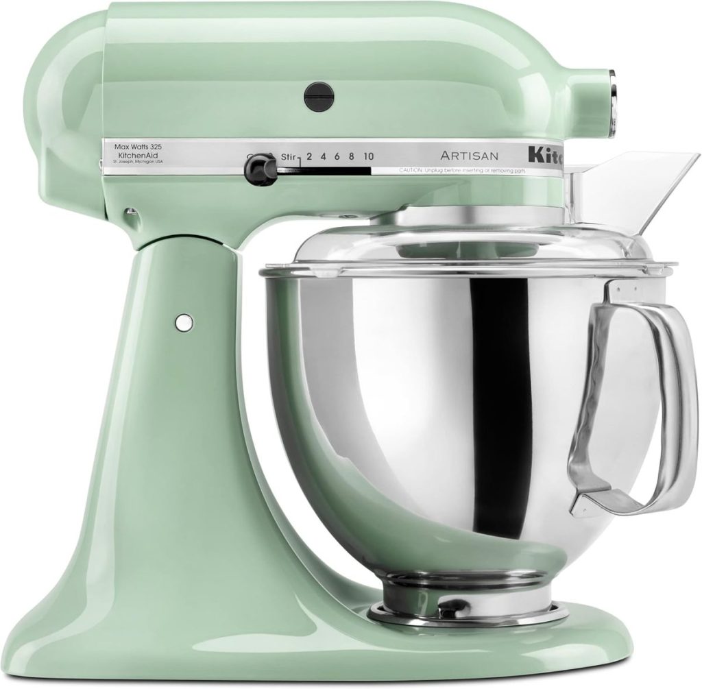 A mint green KitchenAid stand mixer with a stainless steel mixing bowl and attached pouring shield, perfect for whipping up a flower cake, viewed from the side.