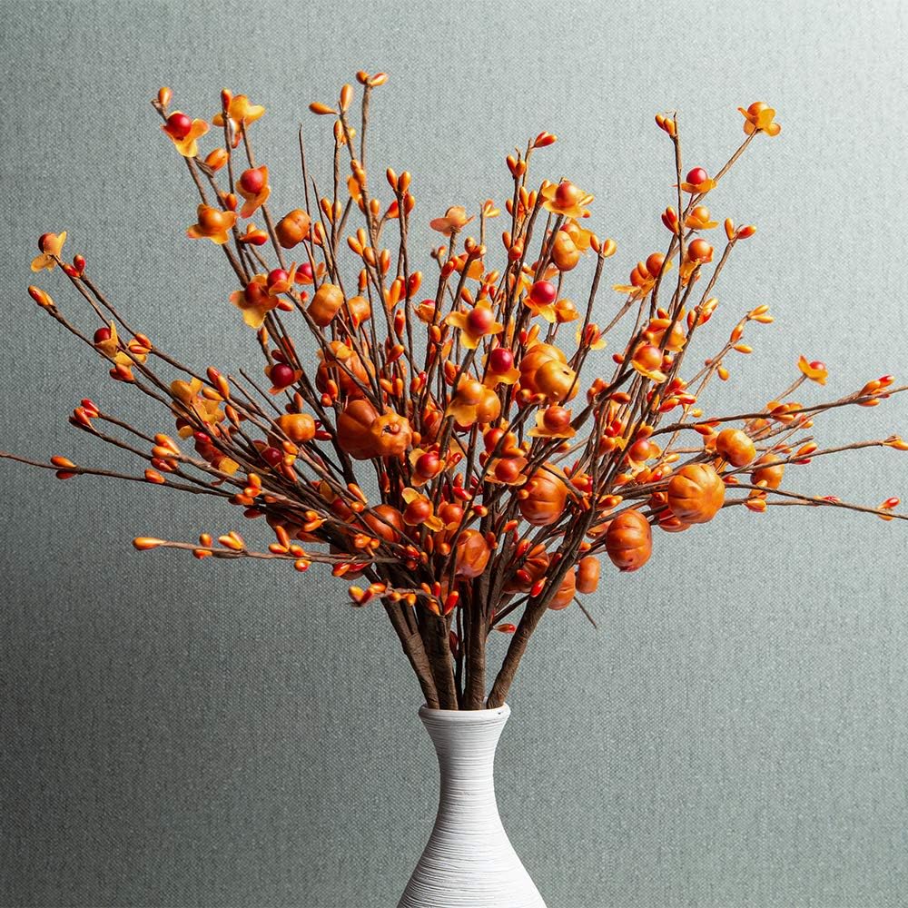 A white vase holds orange and yellow artificial branches with small leaves and berries, creating a cozy touch of fall home decor against a textured gray background.