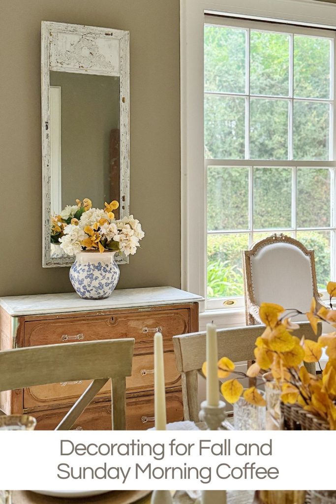 A wooden dining table with fall-themed floral arrangements in a rustic vase, lit by natural light from a large window. A mirror and chest of drawers are against the wall. Caption reads: "Decorating for Fall and Sunday Morning Coffee".