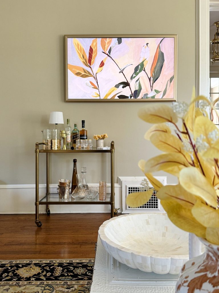 A living room scene features a bar cart with drinks and glasses, a floral artwork on the wall, and a decorative bowl in the foreground.