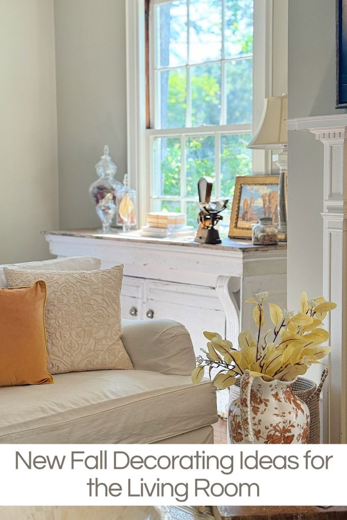 A cozy living room with light decor, featuring a white sofa with orange and beige cushions, a sideboard with decor items and a window. Text reads, "New Fall Decorating Ideas for the Living Room.