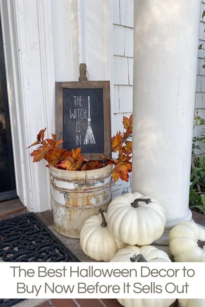 A porch with white pumpkins, an old bucket filled with autumn leaves, and a framed chalkboard sign reading "The Witch Is In." Text below the image reads, "The Best Halloween Décor to Buy Now Before It Sells Out.