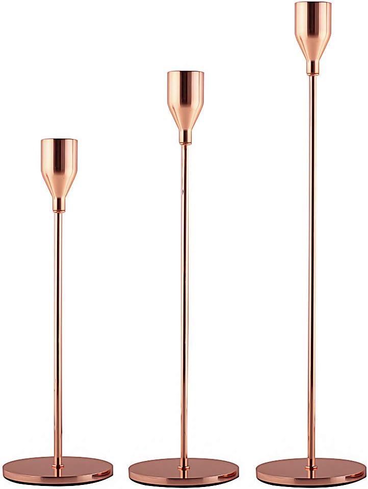 Three copper-colored metal candle holders of varying heights stand gracefully on a white background, perfect for complementing fall flower arrangements.