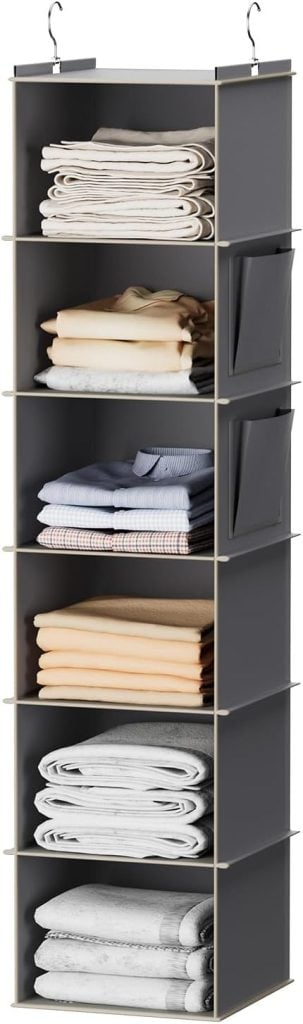 A hanging closet organizer with five shelves containing neatly folded clothes and two gray storage bins.