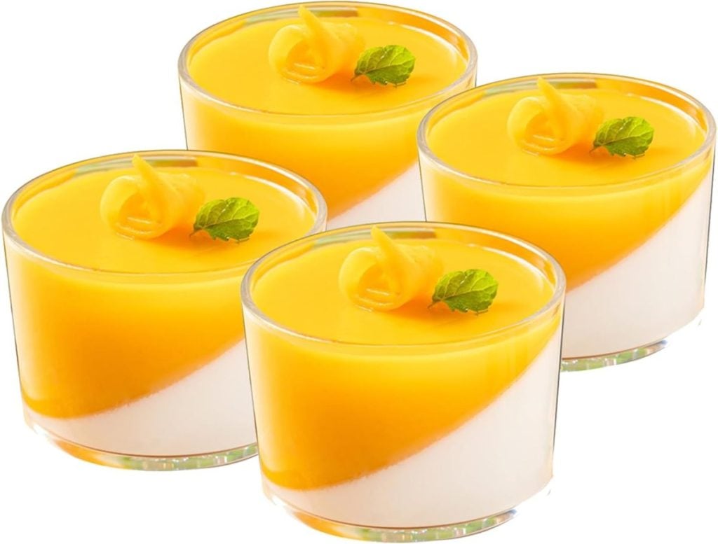 Four small glass cups filled with a two-layered dessert, featuring a white base and a vibrant yellow top layer, garnished with a mint leaf and decorative swirl.