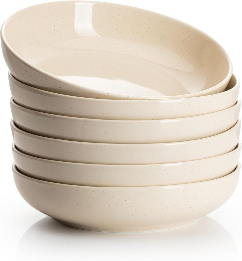 A stack of six beige ceramic bowls, slightly speckled, arranged on a white surface—perfect for serving a fresh harvest salad.