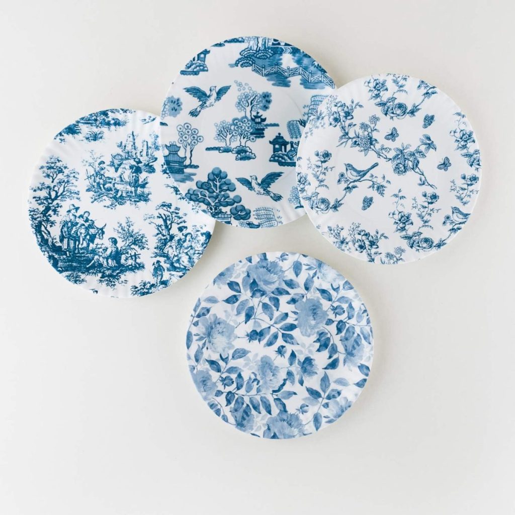 Four decorative plates with blue patterns, including floral and scenic designs, displayed on a white background, beautifully complemented by wood charger plates.