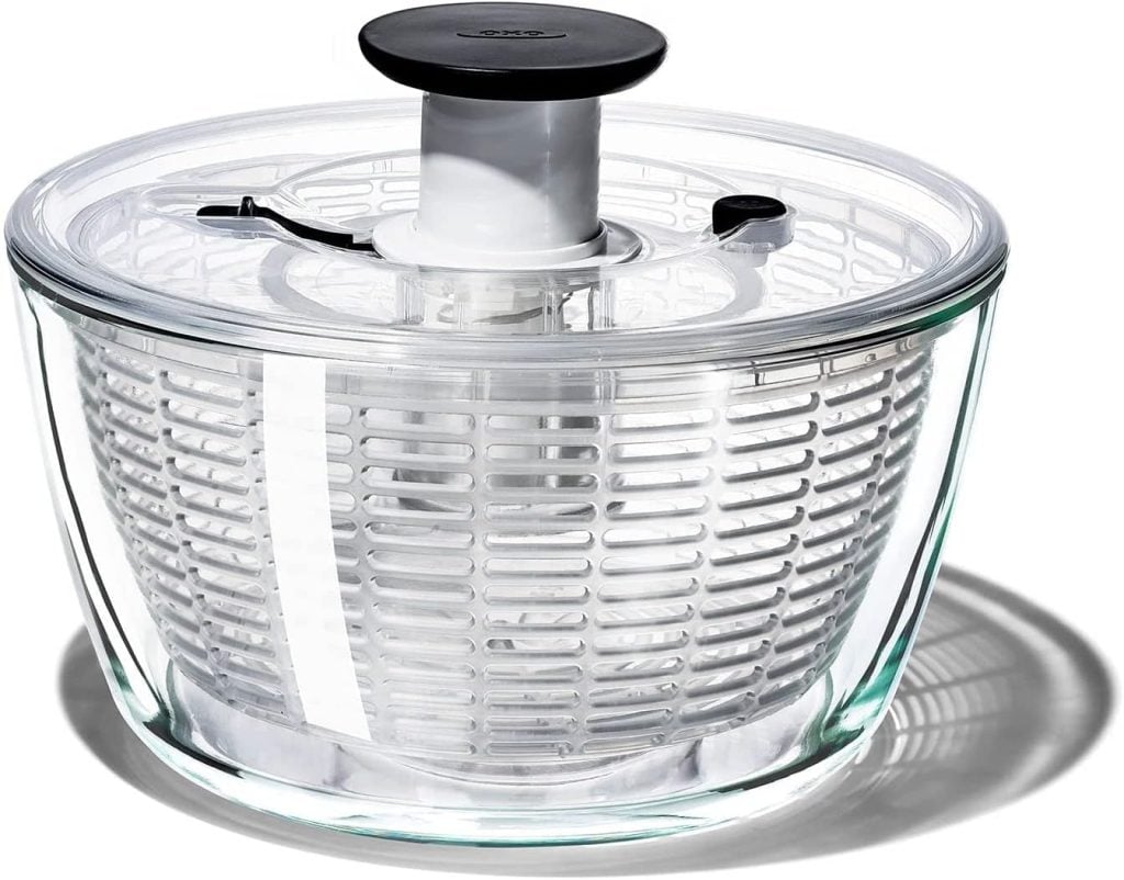 A clear glass salad spinner with a white and black pump handle and an inner plastic strainer basket, perfect for prepping your favorite Harvest Salad, placed on a white background.