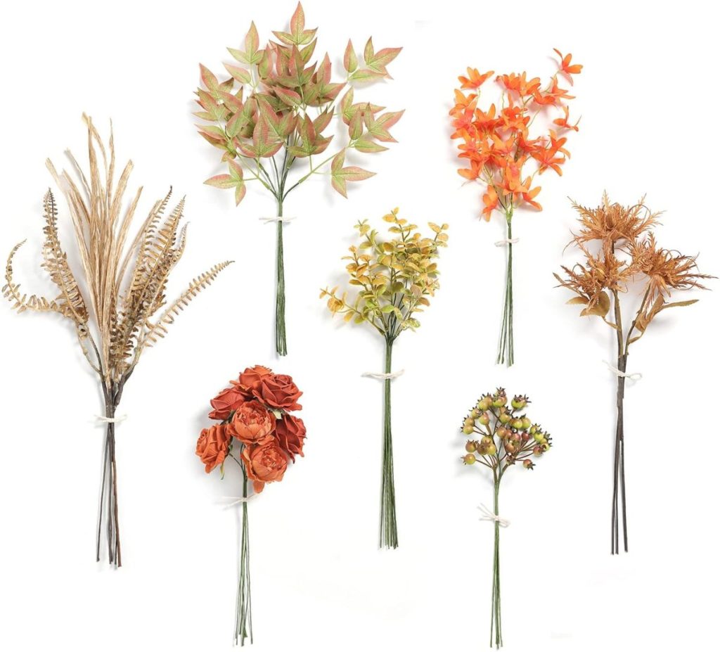 Seven bundles of artificial autumn-themed flowers and foliage, accented with fall pumpkins and tied with white string, arranged in a grid on a white background.