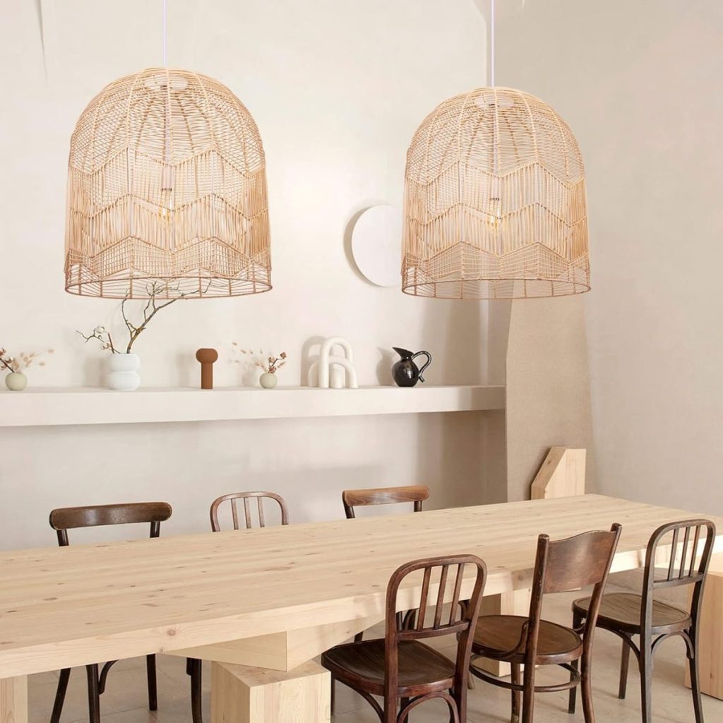 A minimalist dining room features a wooden table with six mismatched chairs and two large wicker pendant lights. A shelf in the background displays minimal decorations, including vases and small sculptures.