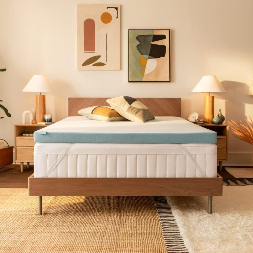 A modern bedroom featuring a wooden bed with a teal mattress topper, abstract artwork on the wall, and two bedside tables with lamps. Decorative pillows are arranged on the bed.