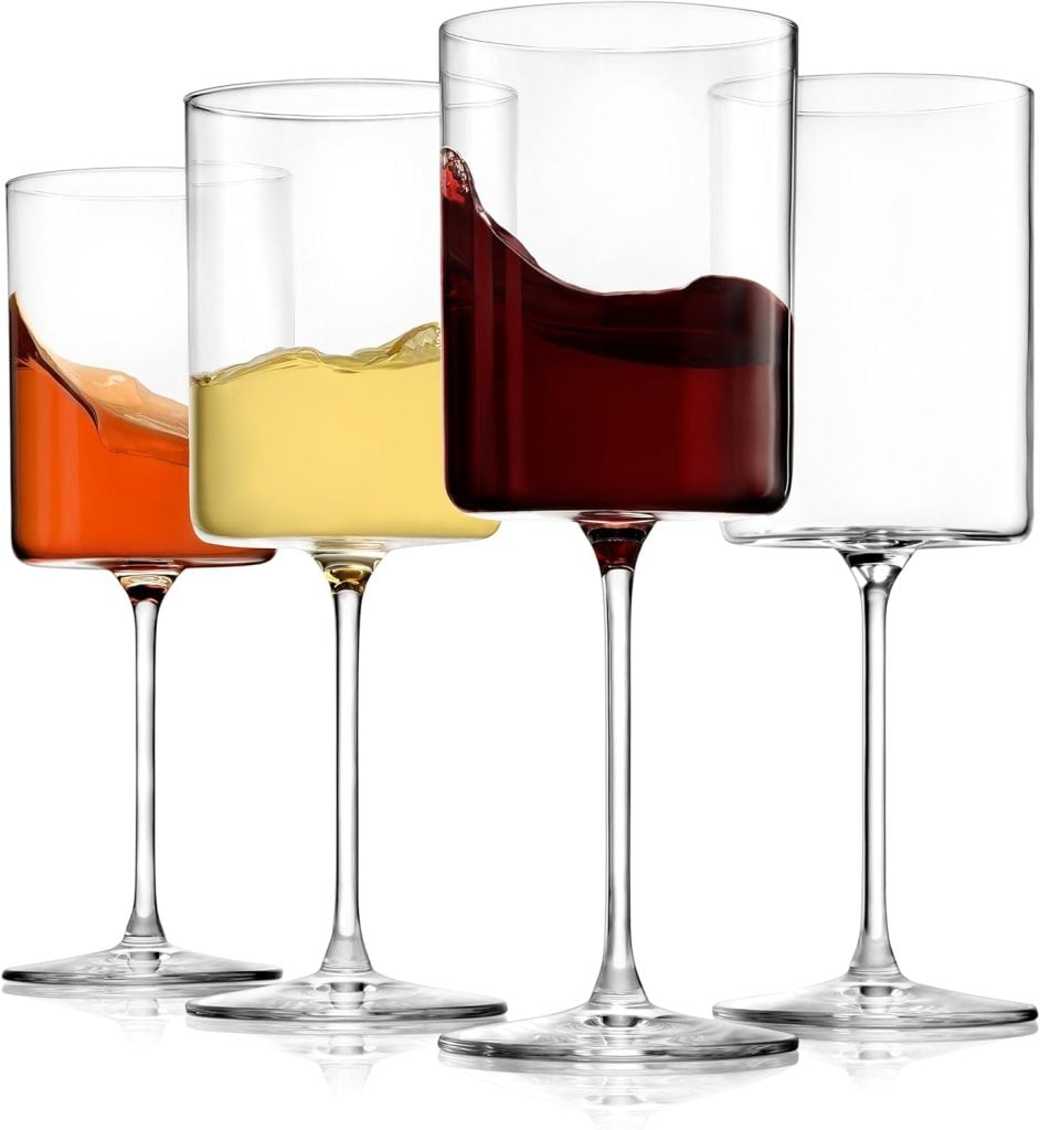 Four clear glasses, each containing different colored liquids: one with an amber liquid, one with a yellow liquid, and two with red liquids, reminiscent of vibrant fall flower arrangements, arranged in a row from left to right.