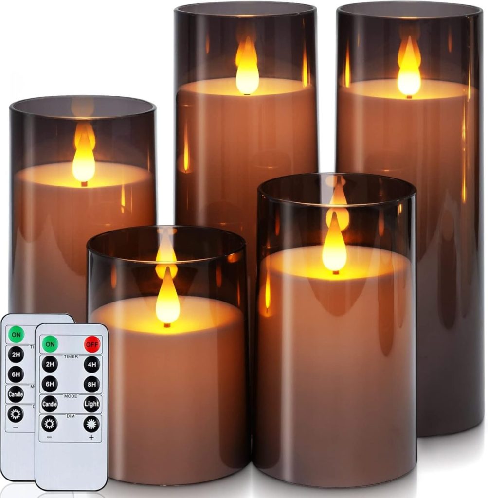 Five battery-operated LED candles with realistic flame effect inside dark smoke-colored glass holders. A remote control with various timing and light settings is placed next to the candles.