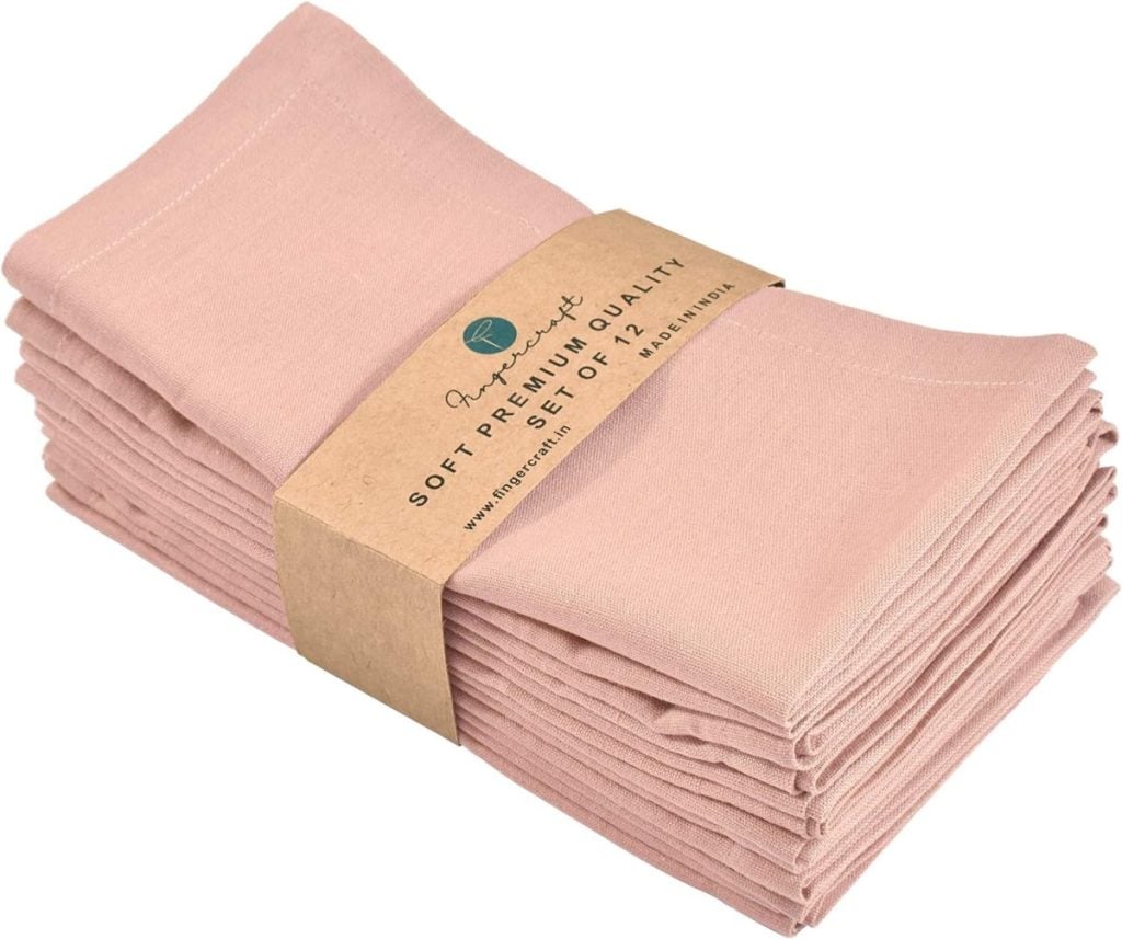 A stack of pink cloth napkins wrapped with a brown paper band that reads "Soft Premium Quality" and "Set of 12," perfect for pairing with wood charger plates.