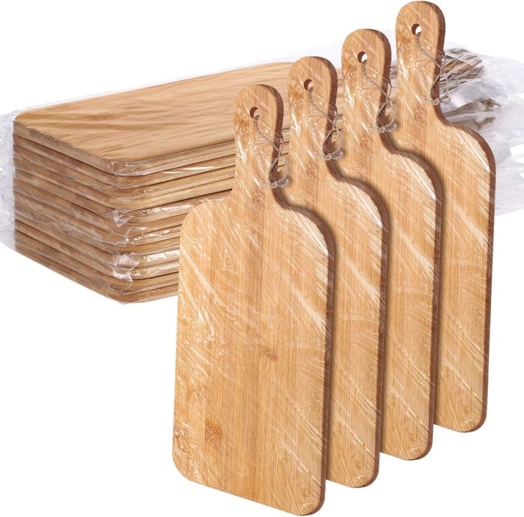 A set of wooden cutting boards with handles, partially wrapped in plastic packaging, displayed in two vertical stacks, alongside elegant plate chargers.