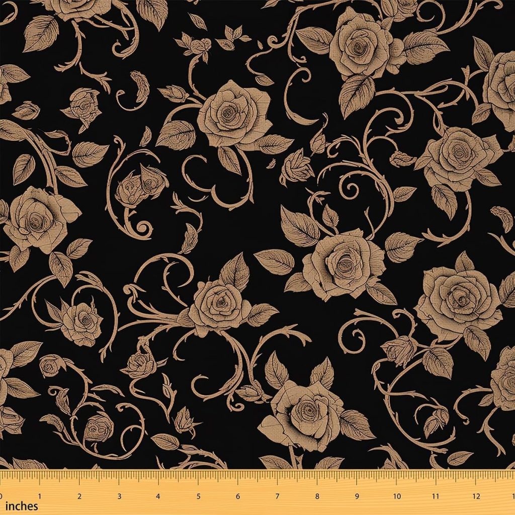 A black fabric with a beige floral rose and vine pattern, accented with hints of fall pumpkins, displayed with a yellow inch ruler along the bottom edge for scale.