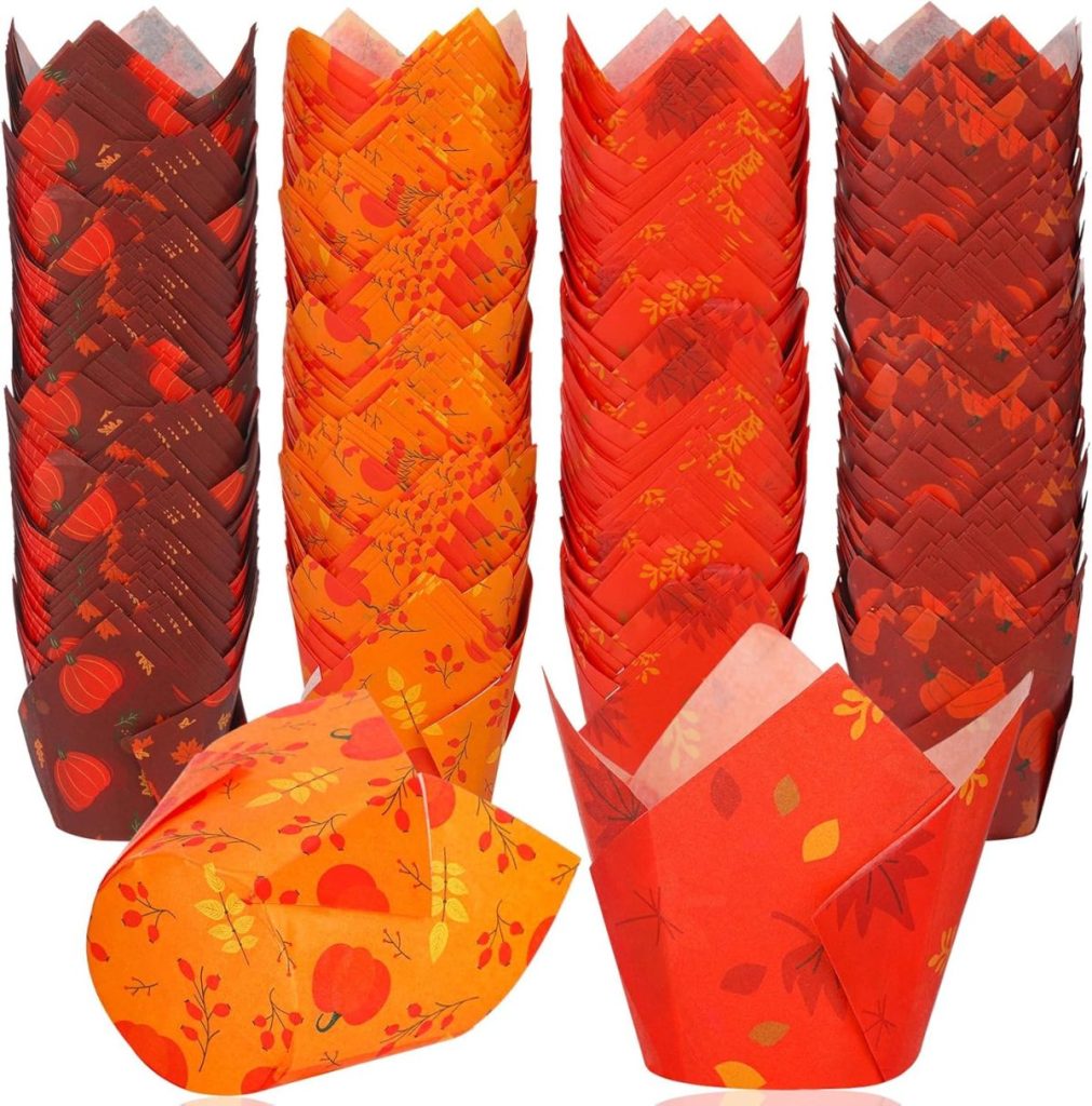 An assortment of red, orange, and brown tulip-style paper muffin liners with autumn-themed designs displayed in multiple stacks, perfect for showcasing your favorite cupcake recipes.