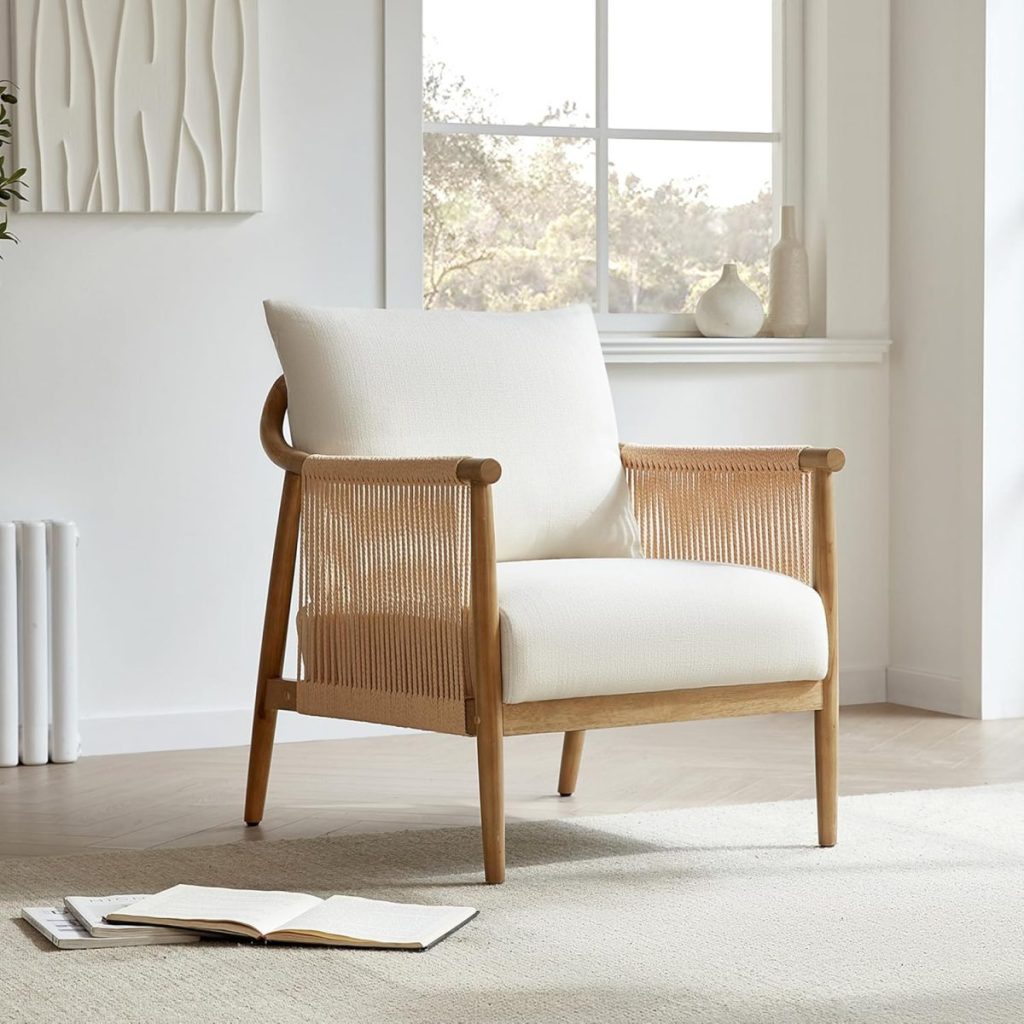 A wooden chair with white cushions is placed by a window in a bright room. An open book lies on the floor in front of the chair.