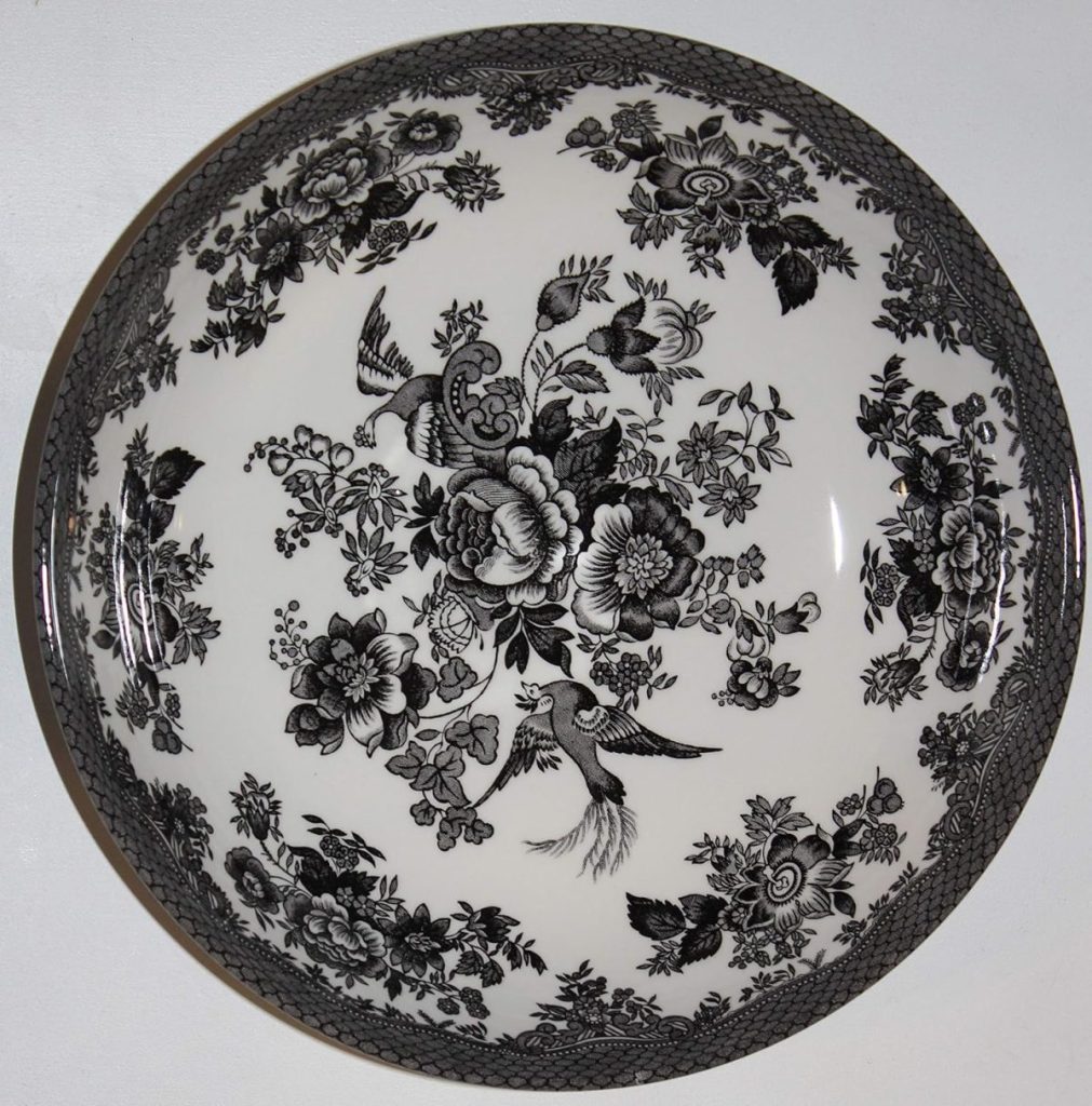A round white ceramic plate with an intricate black floral and bird pattern, bordered by a detailed black design around the edge—perfect for adding charm to any farmhouse table setting.