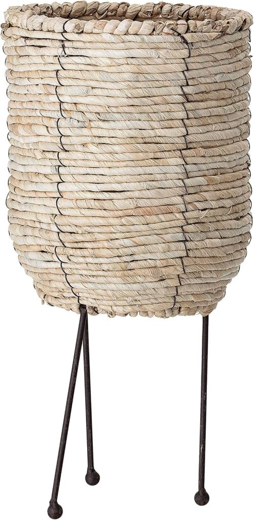 A woven wicker planter basket with a cylindrical shape, featuring black metal tripod legs and a natural beige color—perfect for displaying your favorite fall pumpkin indoors.