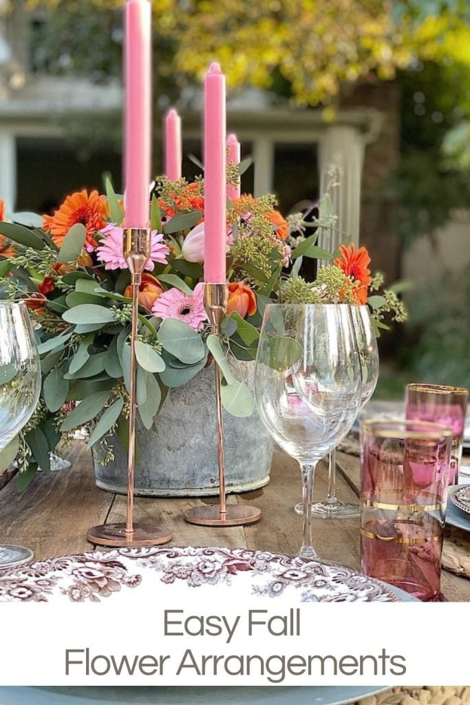 Table setting with pink candles, glassware, and a floral centerpiece with pink and orange flowers. Text overlay reads "Easy Fall Flower Arrangements.