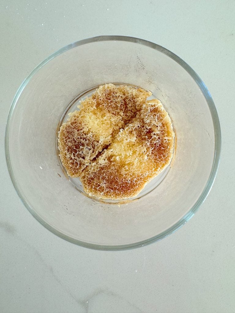 A round piece of honeycomb inside a clear glass bowl, set on a light-colored surface.