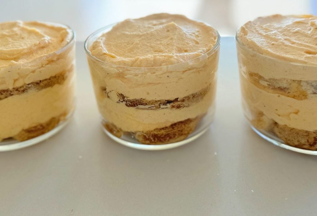 Three glass containers filled with layered tiramisu dessert featuring creamy layers and sponge cake.