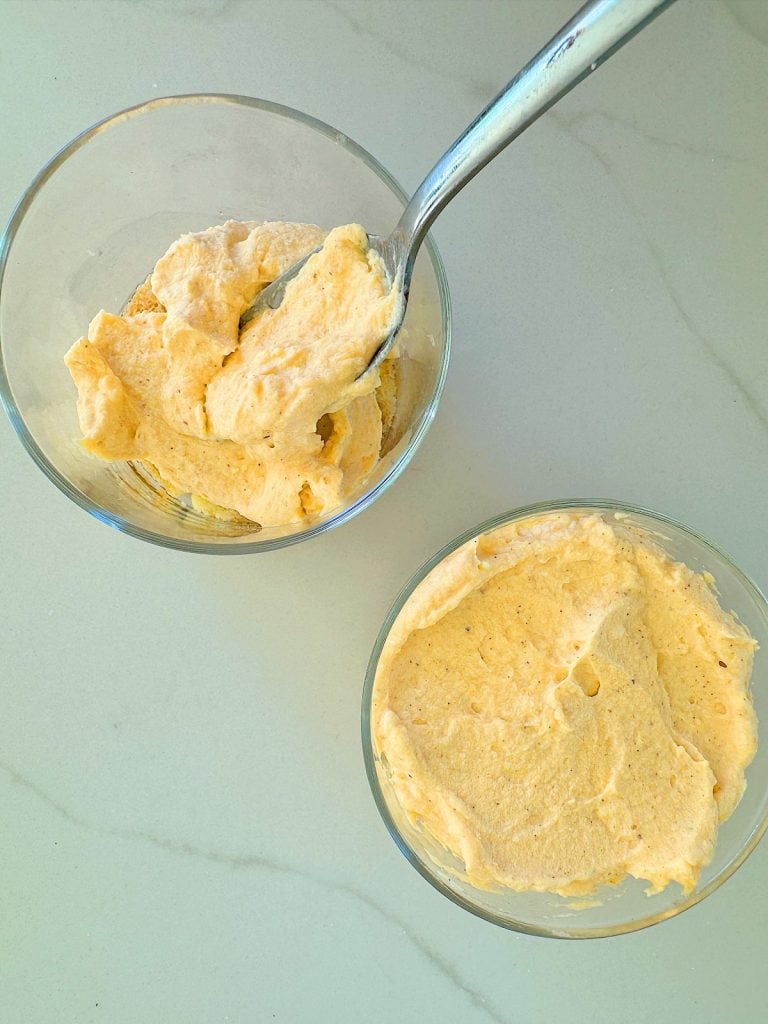 Two bowls of creamy, light-colored mousse with a spoon in one of the bowls, placed on a light-colored surface.