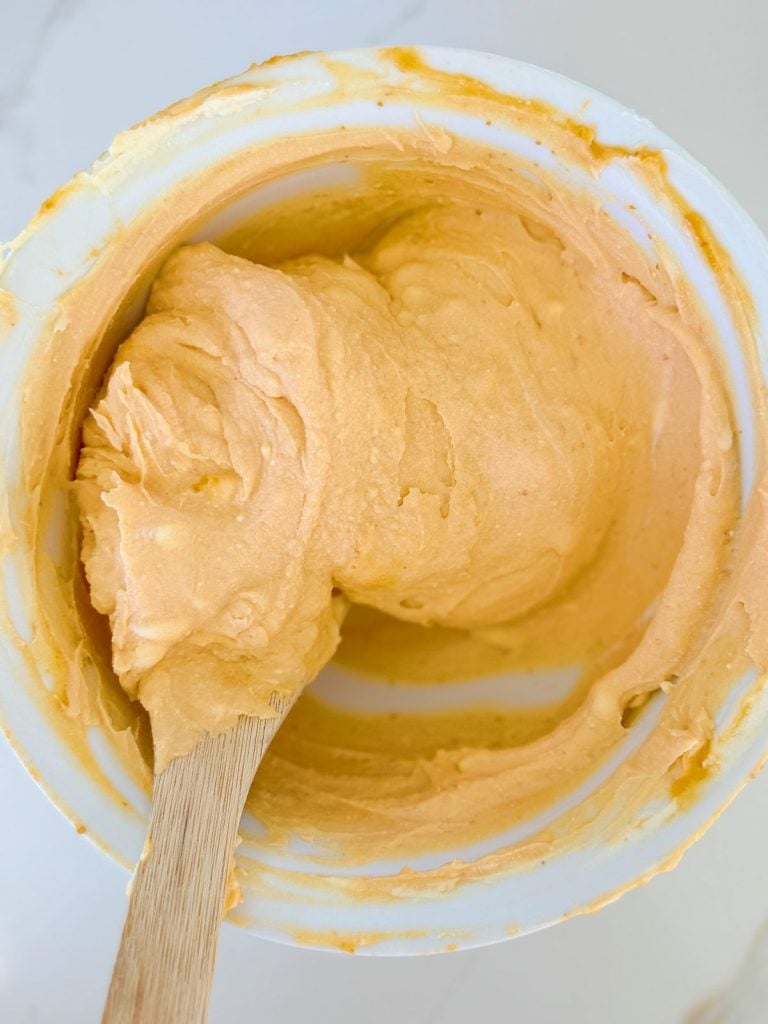 A mixing bowl filled with creamy, orange-hued batter and a wooden spatula nestled inside.