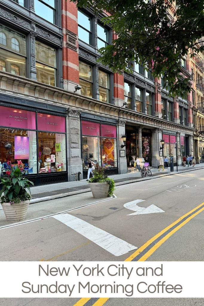 A street in New York City with a large building featuring shops on the ground floor. Pink sale signs are visible in some windows. The street is fairly empty with a few pedestrians and cyclists.