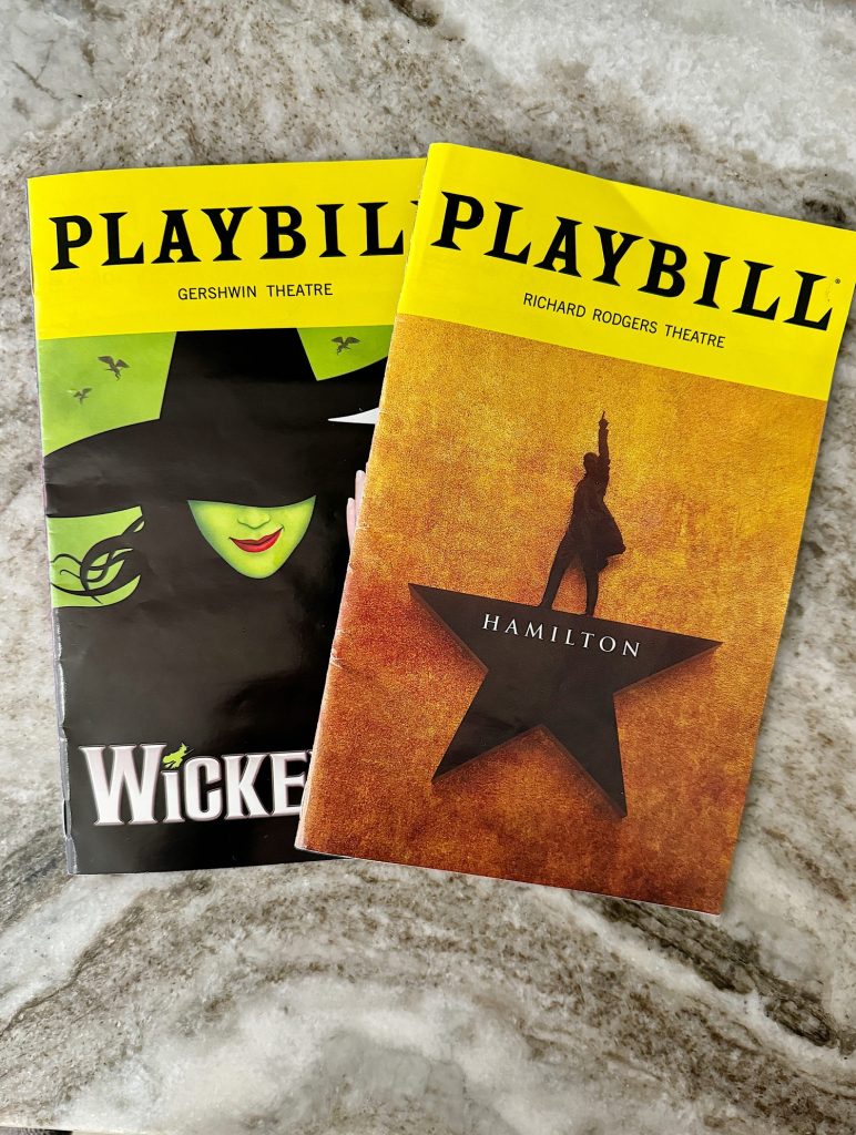 Two Playbill booklets are shown. One is for the Gershwin Theatre's production of "Wicked," featuring a witch illustration. The other is for the Richard Rodgers Theatre's production of "Hamilton," featuring a star silhouette.