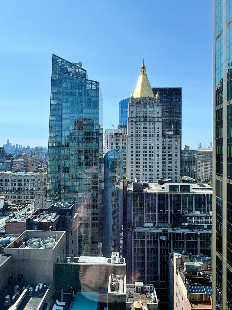 View of a cityscape featuring a distinctive gold-roofed building surrounded by modern glass and concrete structures under a clear blue sky.