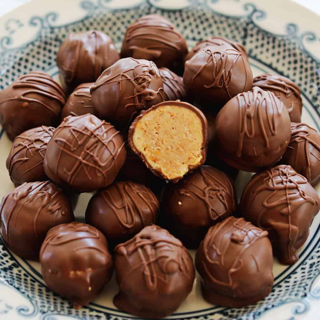 A plate filled with round, chocolate-coated candies, with one candy cut in half to reveal a peanut butter filling. The candies are drizzled with additional chocolate on top.