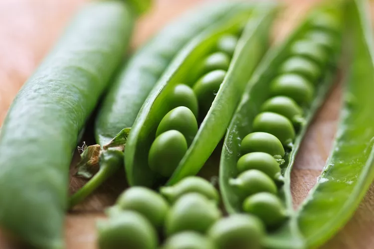 Close-up of opened and unopened green pea pods on a wooden surface, showing fresh peas inside.