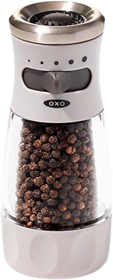 A manual pepper grinder filled with peppercorns, featuring a clear container and a stainless steel top, available now with fast delivery through Amazon Prime.