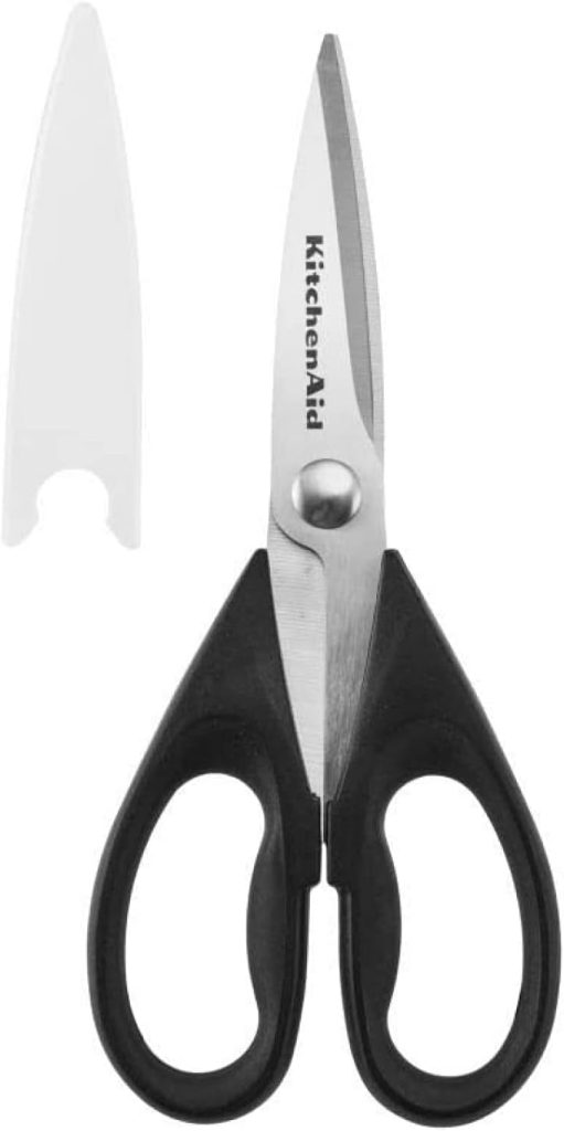 A pair of KitchenAid black-handled kitchen scissors with a white blade cover placed next to them, perfect for prepping your baked brie with jam.