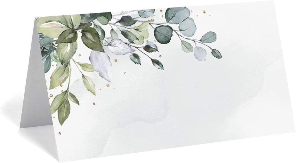 A folded greeting card displaying a botanical design with green leaves and small gold dots on a light background, reminiscent of elegant Thanksgiving plates.