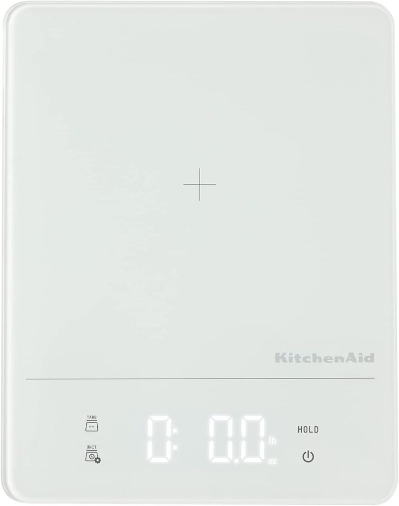 Digital kitchen scale with a white surface and a small display showing "0.0 lb" at the bottom. The brand name KitchenAid is visible on the right side.