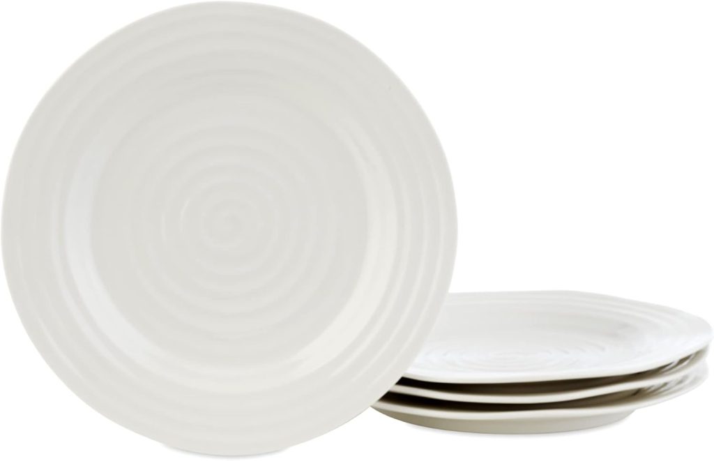 Four white ceramic plates with concentric circle patterns are stacked, with one plate standing upright beside them, complemented by sleek glass water bottles nearby.