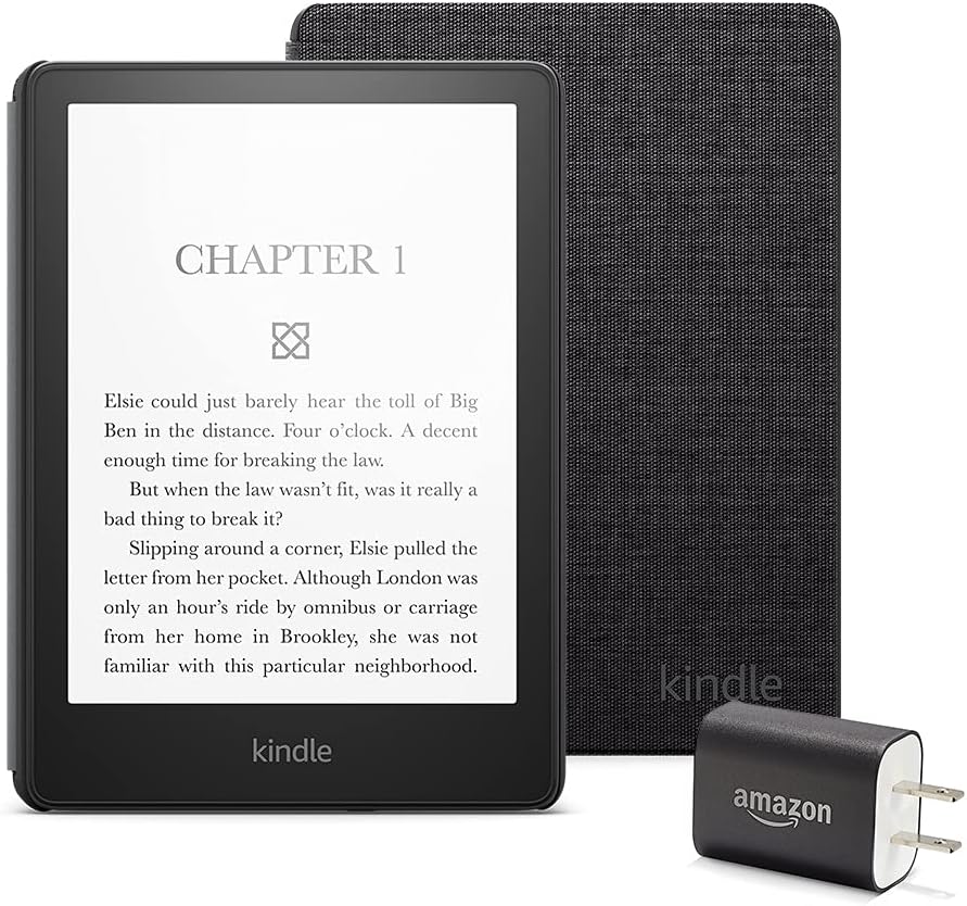 Kindle device displaying a book's first chapter text, with a fabric cover and an Amazon-branded charging adapter beside it.