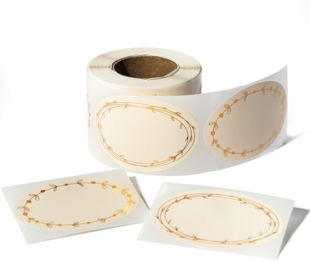 A roll of decorative labels with a gold border featuring leaf patterns, perfect for adding a touch of elegance to glass water bottles, accompanied by two individual labels.