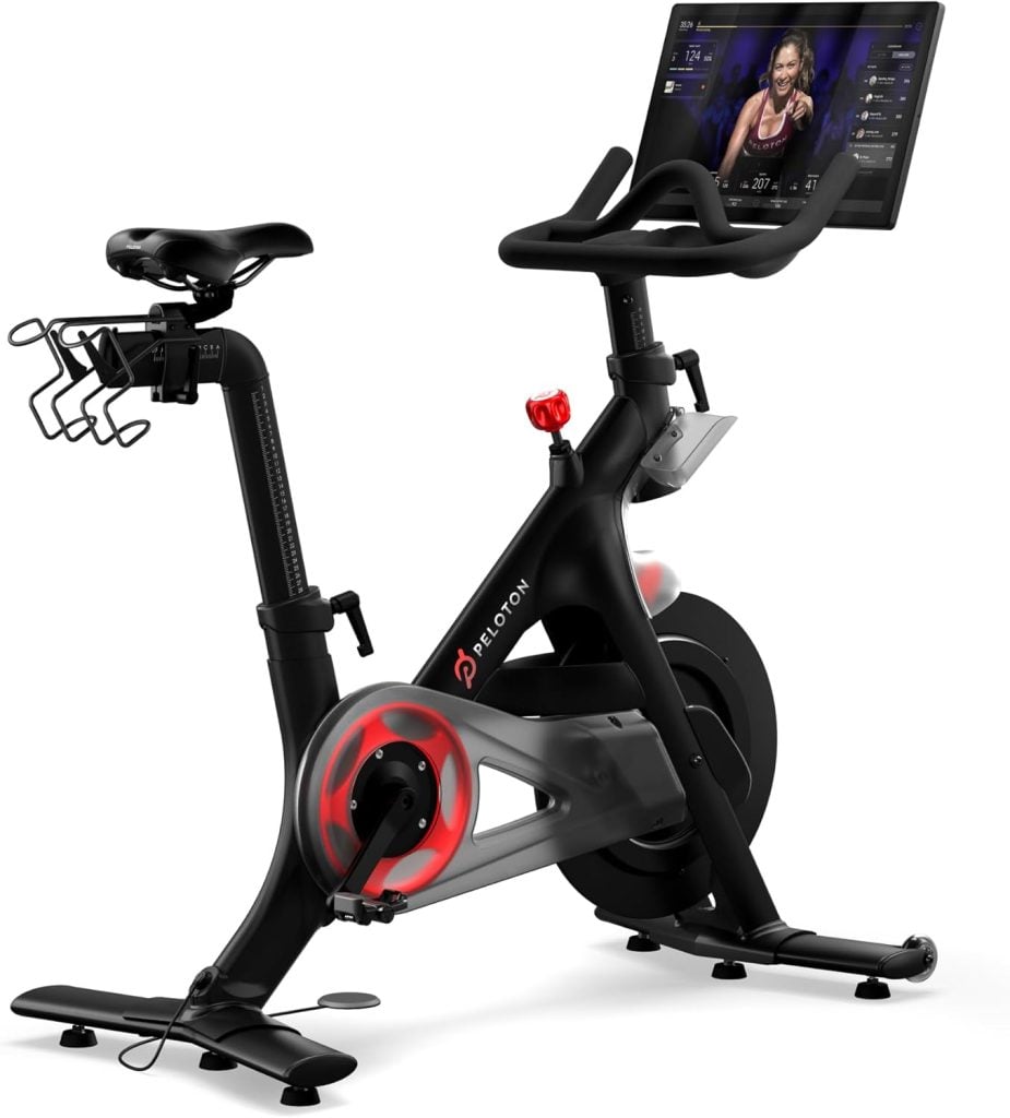 A stationary exercise bike with a digital screen displaying a workout class, featuring a water bottle holder and adjustable seat.