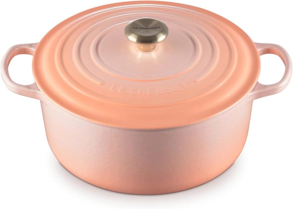 A round peach-colored Le Creuset Dutch oven with a gold knob and handles on both sides.