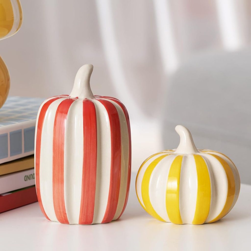 Two ceramic pumpkins with vertical stripes, one red and tall, the other yellow and short, placed on a stack of books.