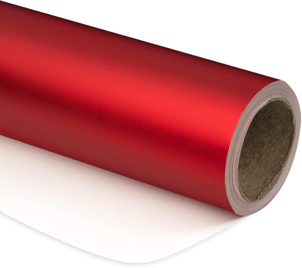 A roll of shiny red wrapping paper with a white underside, partially unrolled and placed on a white surface.