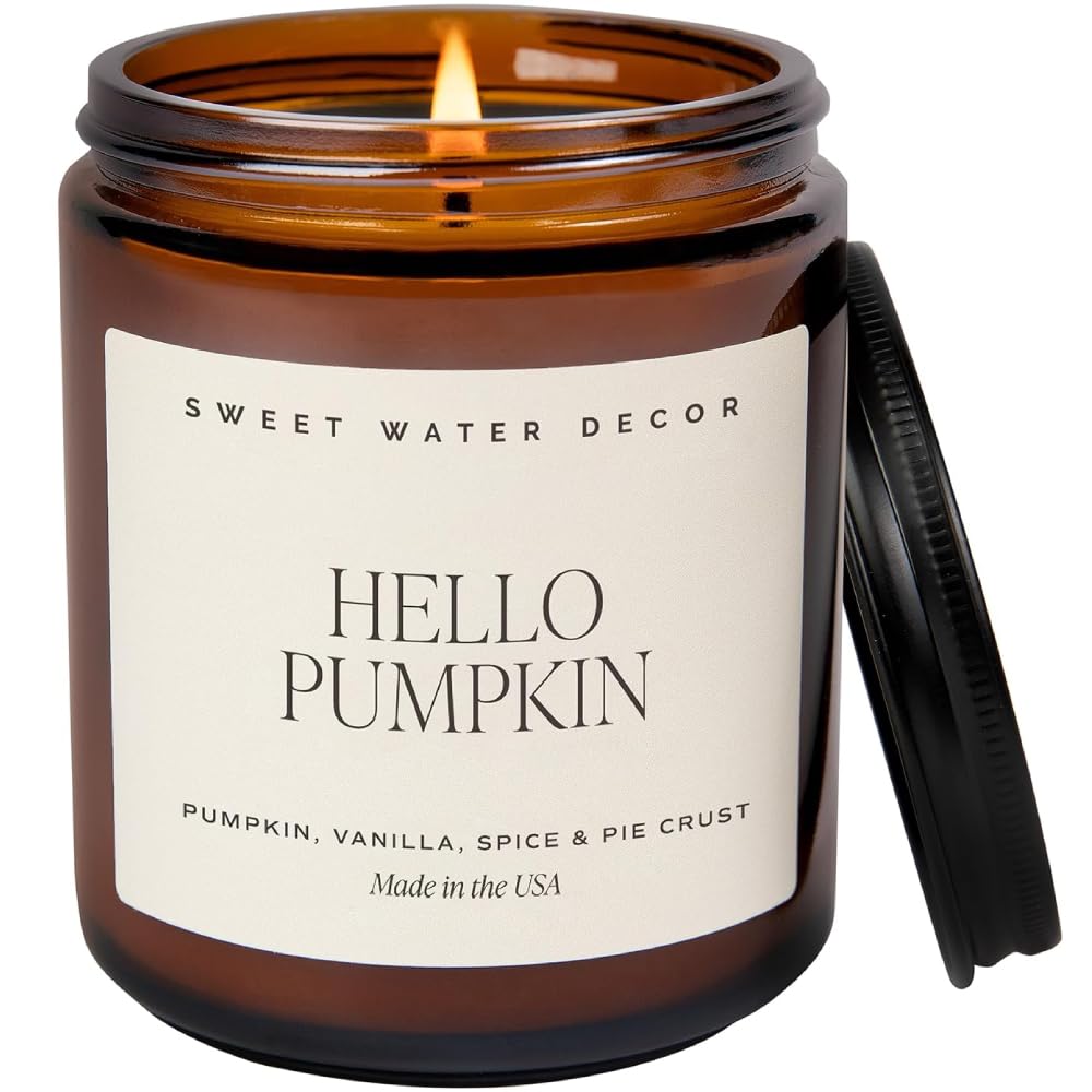 Brown glass jar candle with label reading "HELLO PUMPKIN" and description of pumpkin, vanilla, spice, and pie crust scent. Lid is off, showing a lit wick. Made by Sweet Water Decor.